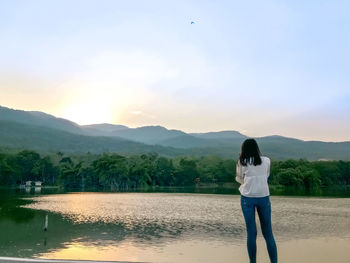 Rear view of woman standing on mountain against sky during sunset