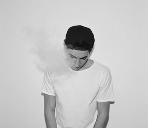 Teenage boy looking down while standing by smoke against white background