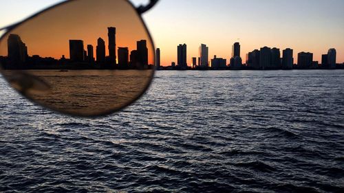 Silhouette buildings by river seen through sunglasses during sunset