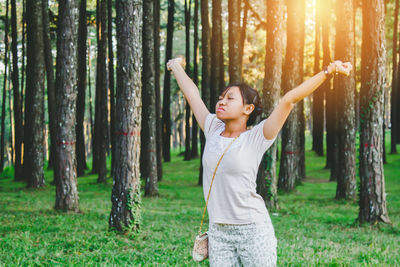 Young woman with arms outstretched standing against trees in forest