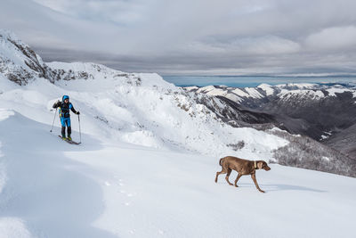 Man with dog snowboarding on snowcapped mountain against sky