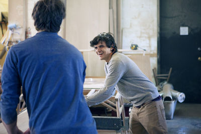 Happy carpenter talking to colleague while working in workshop