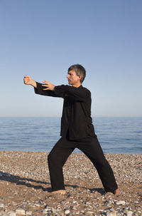 Mature man practicing tai chi at beach against clear blue sky