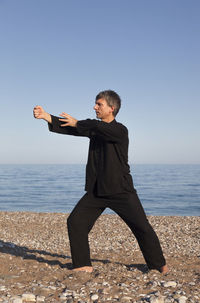 Mature man practicing martial arts at beach against sky
