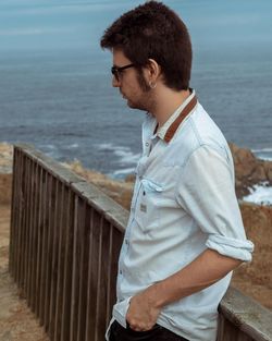 Side view of young man standing on retaining wall by sea