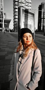 Portrait of young woman standing against building in city