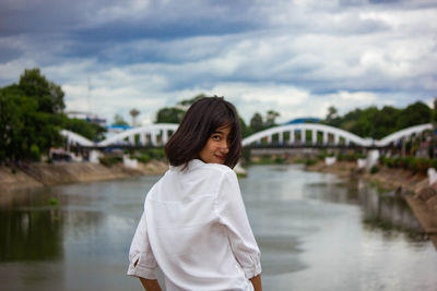 Girl standing on bridge over river against sky