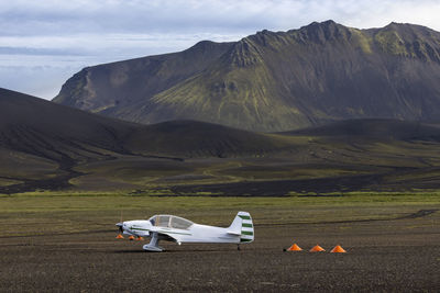 White monoplane parked on spacious grassy valley surrounded by rough picturesque mountain range in nordic nature