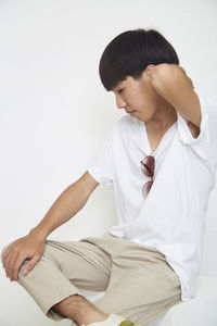 Young man looking away while sitting against white background