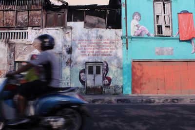 Blurred motion of people riding motorcycle on street against buildings in city