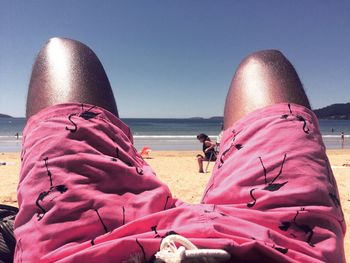 Midsection of man relaxing at beach against sky on sunny day