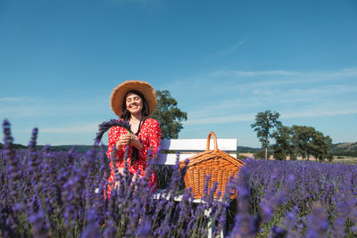 Portrait of woman standing amidst flowering plants on field against sky