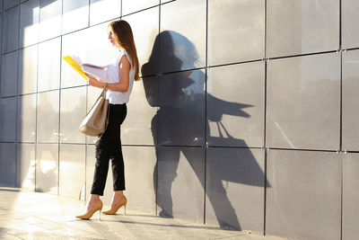 Businesswoman reading document while standing against wall