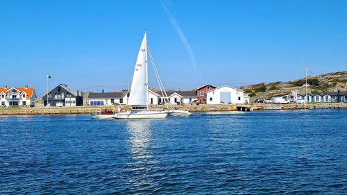 Sailboats in sea by buildings against clear blue sky