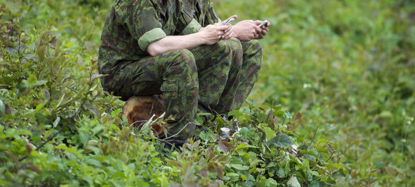 Low section of army soldiers using phones while sitting on green field