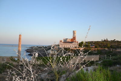 Buildings by sea against clear blue sky