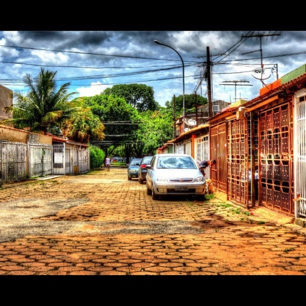 transportation, land vehicle, sky, mode of transport, car, building exterior, architecture, tree, built structure, street, road, cloud - sky, transfer print, cloud, auto post production filter, city, on the move, house, outdoors, cloudy