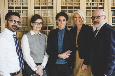 Portrait of confident lawyers standing against bookshelf