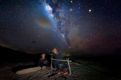 Father and son preparing food on bonfire against sky