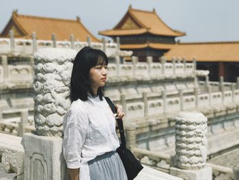 Young woman standing outside temple against clear sky