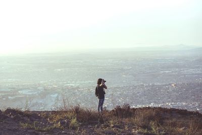 Woman photographing through camera while standing on mountain