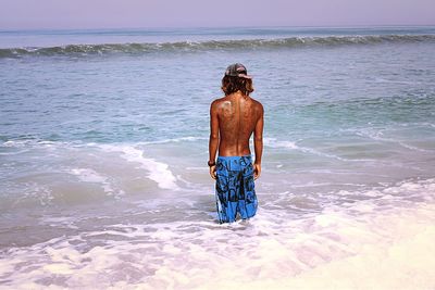 Rear view of shirtless man walking on beach