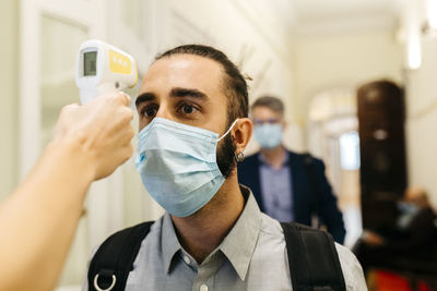 Hand of female with infrared thermometer checking businessman's temperature in corridor