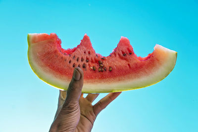 Close-up of hand holding a watermelon against blue sky