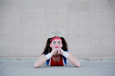 Portrait of young woman in sports clothing lying against wall