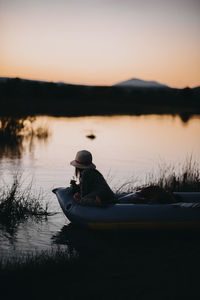 Girl sitting in inflatable raft on lake against clear sky during sunset