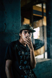 Portrait of young man smoking cigarette against wall