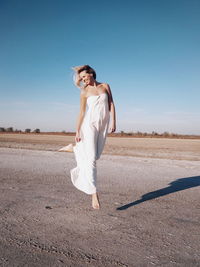 Woman in dress jumping on field against clear sky