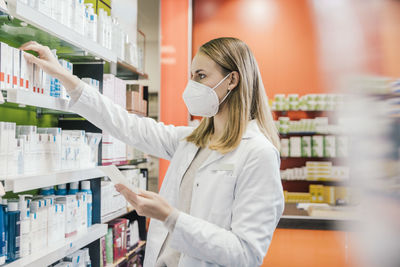 Female pharmacist wearing protective face mask while working in chemist shop