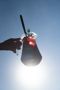 Low angle view of hand holding umbrella against clear blue sky