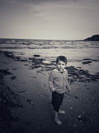 Boy standing on beach against sky