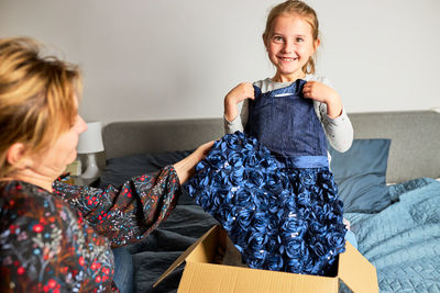 Mother and her daughter opening box with ordered dress at home on couch