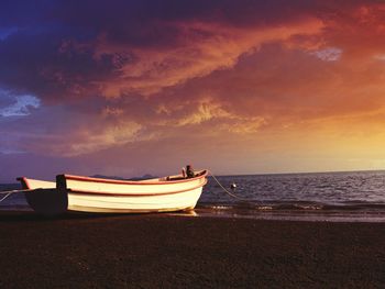 Boat moored on shore against sky during sunset