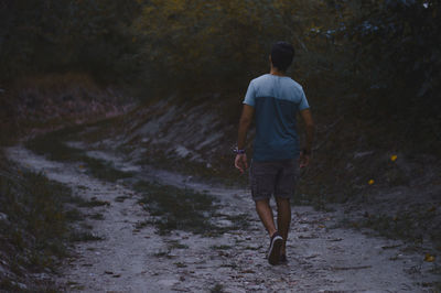 Full length rear view of man walking on dirt road