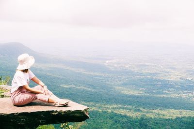 Man sitting on mountain by lake against sky