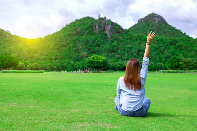 Rear view of woman sitting on grass against trees