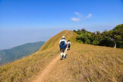 Rear view of people hiking on landscape against sky