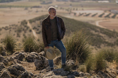 Portrait of adult man with brown leather jacket standing on top of hill