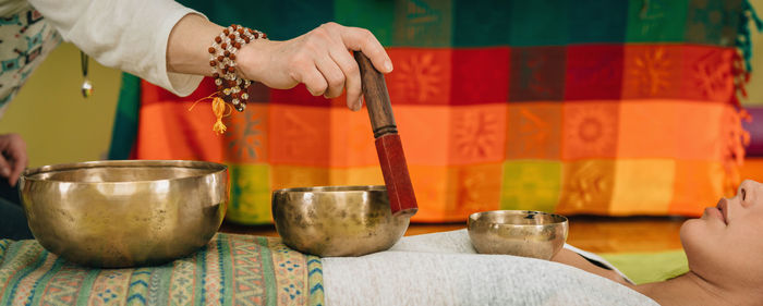 Cropped hand of therapist playing rin gong on young woman at spa