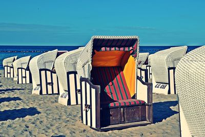 Hooded chairs on beach against blue sky