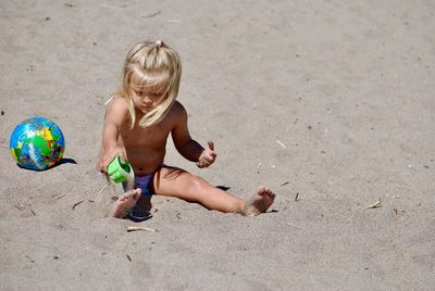 Shirtless girl playing with toy while sitting on sand at beach during sunny day