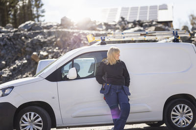 Female electrician leaning on van during sunny day