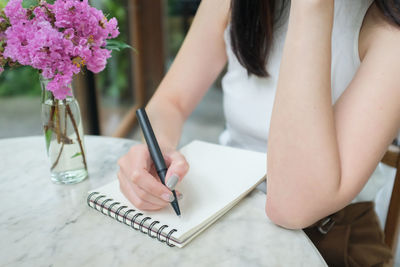 Midsection of woman writing in book at table