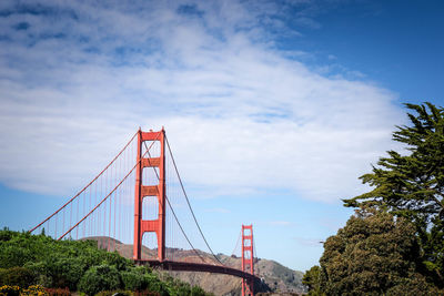 Low angle view of suspension bridge against cloudy sky