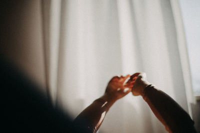 Cropped hands against curtain at home