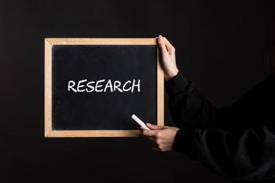 Midsection of man holding blackboard against black background